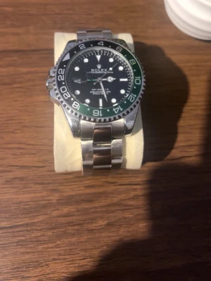 Klocka - Klocka med silverfärgad länk i rostfritt stål och svart urtavla. Klockan har en grön och svart vridbar bezel med vita markeringar och tydliga visare. Perfekt accessoar för dig som gillar klassisk och exklusiv stil. Den är helt ny, utan skador och funkar perfekt. Priset kan diskuteras!