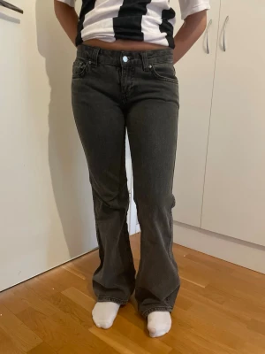 Mörkgrå bootcut jeans - Mörkgrå färg Säljer ett par mörkgrå bootcut jeans med låg midja och klassiska fem fickor. Jeansen har snygga ficklock med knapp bak och är tillverkade i ett mjukt denimtyg. Perfekta för en avslappnad och trendig look.