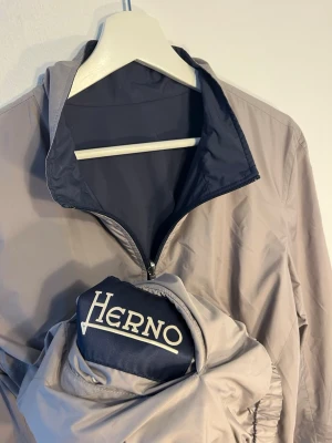 Herno jacka - Sjukt fet vändbar jacka från Herno. Tunn och lätt. Kan vara mörkblå eller grå. Kostar ca 4000kr ny. Jackan kan packas ihop i sin egen ficka. Storlek 48 men passar som S