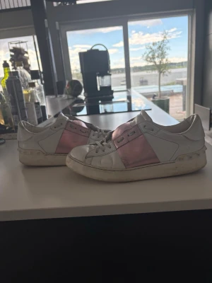 Valentino Garavani vita sneakers rosa - Snygga vita sneakers från Valentino Garavani med bred metallicrosa rem över mitten. Säljer för att dom inte används. Storlek: 39 