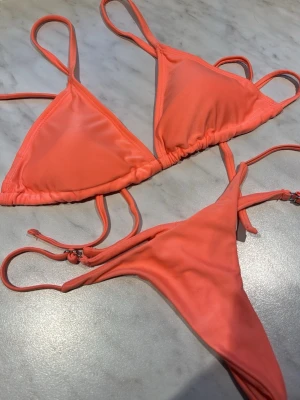 Korallfärgad bikini med knyt - Snygg trekantsbikini i korallrosa med smala axelband och justerbara knyt i både topp och trosa. Klassisk modell som ger en fräsch look på stranden. Materialet känns mjukt och följsamt, perfekt för soliga dagar.