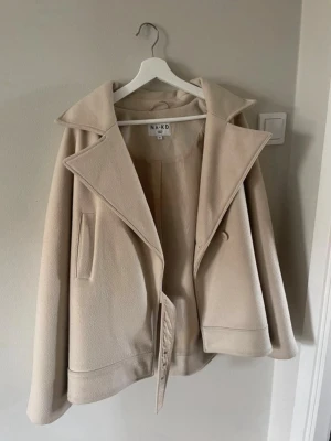 Beige kappa från NA-KD med bred krage - Beige kappa från NA-KD med bred krage och knäppning framtill. Storlek S men den är större i modellen så skulle säga mer som strl M. Använd fåtal gånger