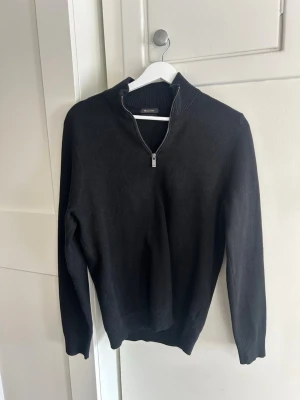 Svart halvzip tröja från Massimo Dutii - Klassisk svart tröja från Massimo Dutti med halv dragkedja och hög krage. Tröjan har långa ärmar, ribbade muddar och är tillverkad i mjukt material som passar perfekt till lager på lager. Enkel och stilren design som funkar till det mesta.