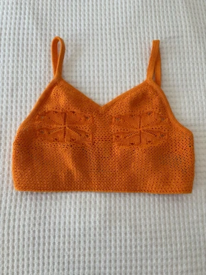 Orange stickad linnetopp - Superfin orange stickad linnetopp med smala axelband och snyggt virkat mönster framtill. Perfekt för varma dagar och ger en cool, avslappnad vibe. Toppen är ärmlös och har en croppad passform.