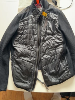 Svart vindjacka från Napapijri - Snygg svart vindjacka från parajumper med quiltade partier fram och bak samt stickade ärmar och sidor. Jackan har hög krage, dragkedja framtill och praktiska fickor med dragkedja. Materialmix av polyester och syntet för både stil och funktion. Ny kostar 4199 länken till parajumpersida som bevisar det kostar så https://www.parajumpers.it/se/en/men/clothing/hybrids/jayden---hybrid-jacket-black-26SMPMHYWU01P050541.html 