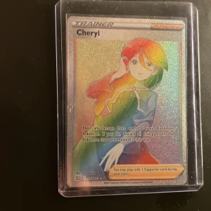 Pokémonkort Cheryl Trainer Supporter - Säljer ett holografiskt Pokémonkort av typen Trainer Supporter med motivet Cheryl. Kortet har regnbågsskimrande yta och ligger i ett genomskinligt plastfodral. Perfekt för samlare eller Pokémonfans som vill utöka sin kortsamling.