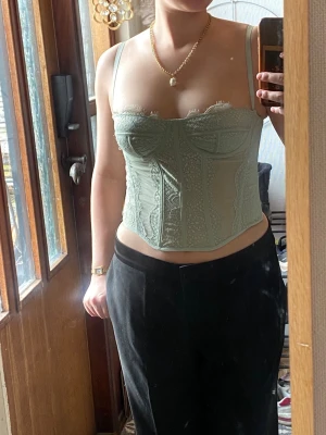 Mintgrön spetskorsett med detaljer - Mintgrön korsett med tunna axelband och vackra spetsdetaljer framtill. Modellen har bygelkupor och dekorativa sömmar som ger en snygg siluett. Köpt på Vinted och tyvärr saknas lapp, märke och storlek. Passar som xs/s och skulle säga att det är A eller B kupa.
