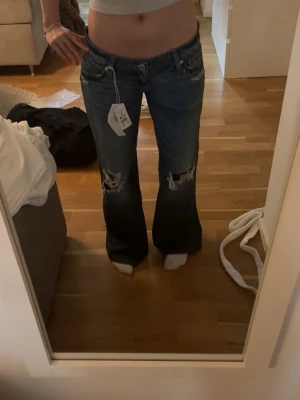 Blå slitna bootcut jeans - Säljer ett par blå baggy jeans med slitningar och hål på knäna från Gina Tricot 14+. Jeansen är i st M tall. Helt nya med lappen kvar❤️