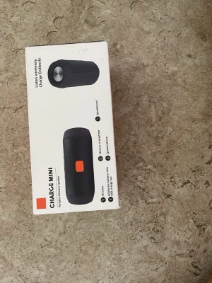 Charge Mini bärbar högtalare svart - Smidig och trådlös bärbar högtalare från Charge i svart färg med cylinderformad design. Högtalaren har en orange detalj och är enkel att ta med sig. Passar till mobil, surfplatta och dator via Bluetooth. Perfekt för att lyssna på musik var du vill.