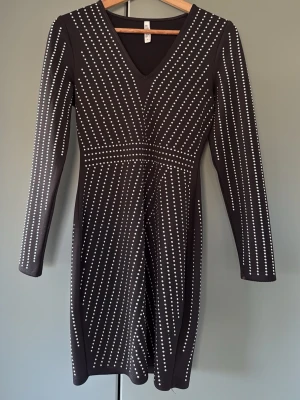 Svart klänning med silverprickar - Snygg svart kortklänning med långa ärmar och v-ringning. Klänningen har ett coolt mönster av silverfärgade prickar i diagonala linjer som ger en unik look. Materialet känns stretchigt och följsamt (scubatyg som håller in på rätta ställen), perfekt för dig som vill sticka ut.