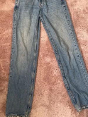 Ljusblå raka jeans från Gina Tricot - Säljer ett par ljusblå raka jeans från Gina Tricot. Klassisk femficksmodell med knappgylf och slitna detaljer vid benslut. Jeansen är i 100% bomull men har även en fläck som inte går bort, se bild 3💕