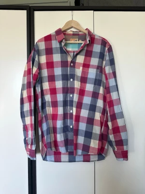 Rutig skjorta i rosa och blått - Säljer en klassisk rutig skjorta med stora rutor i rosa, blått, vitt. Skjortan har långa ärmar, knappar framtill och en bröstficka. Tillverkad i mjuk bomull, perfekt för en avslappnad och trendig stil.