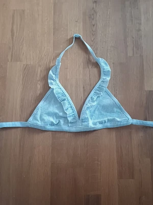 Blåvit randig bikiniöverdel med volang - Supersöt trekantsbikini i blåvitt randigt med volangdetaljer längs kanterna. Knyt i nacken och ryggen för perfekt passform. Perfekt för lata dagar på stranden eller poolhäng med vänner.