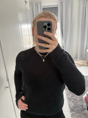 Svart stickad tröja  - Säljer en svart stickad tröja med rund halsringning och grovstickad struktur. Tröjan har långa ärmar och ribbade muddar vid hals, ärmslut och nederkant. Perfekt för lager-på-lager och enkel att matcha med olika outfits.