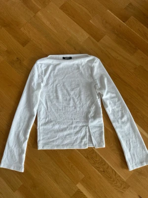 Vit långärmad topp Gina Tricot - Klassisk vit långärmad topp från Gina Tricot i strukturerad bomullsmix. Modellen har en rak passform och en liten slits i sidan för extra detalj. 