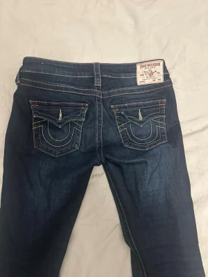 Mörkblå True Religion jeans - True religion jeans i väldigt bra skick, använd ett få tal gånger. I modellen joey. Säljes pga att dom blivit för stora för mig. Uppsydda och passar på en som är ca 170cm lång, storlek 27 (S/36) Nypris 1300kr 