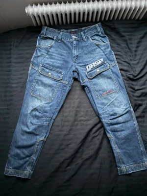 Blå jeans från G-Star RAW - Säljer ett par snygga GASP jeans med cargo-fickor och tryck. Äldre modell som inte längre säljs – lite svårare att få tag på idag.  ✔️ Storlek: [m] ✔️ Färg: Blå denim ✔️ Skick: Bra använt skick (se bilder) ✔️ Rejäla material + flera fickor  Perfekta för dig som gillar GASP, gymstil eller workwear/Y2K. Sticker ut mer än vanliga jeans 🔥midja 42 innerbenslängd 74 ytterlängd 102 måtten kan skiljas med -1 +1cm