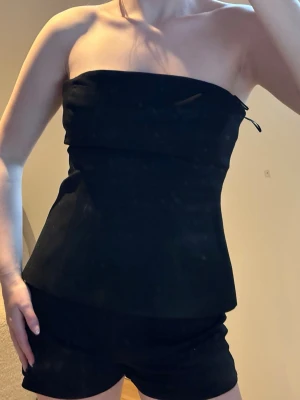 Festtopp  - Snygg svart axelbandslös tubtopp med enkel och stilren design. Toppen har en bandeauformad överdel och sitter tight över bysten. Perfekt att matcha med shorts eller kjol för en clean look. 🎉🌸🌟😍🩷