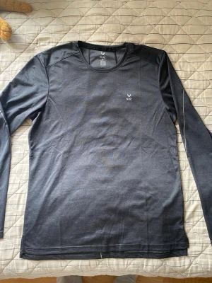 Svart långärmad träningströja SOC - Snygg svart långärmad träningströja från SOC. Tillverkad i ett mjukt och stretchigt funktionsmaterial som andas bra. Perfekt för löpning, gym eller annan träning. Diskret logga på bröstet och rund halsringning.