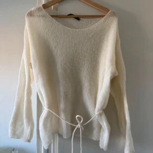 Vit stickad tröja med knyt i midjan - Mysig vit stickad tröja med rund halsringning och långa ärmar. Tröjan har ett knytband i midjan som ger en snygg siluett. 