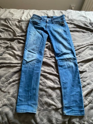 Replay anbass - Säljer ett par blå slim/skinny jeans från Replay, modell Anbass. Jeansen har klassisk femficksdesign, normalhög midja och snygga slitningar. Tillverkade i stretchigt denim för skön passform. Perfekta till en avslappnad och trendig look. Replay lappen bak har en spricka därav priset men syns inte med bälte och knappt när man kör utan bälte. 