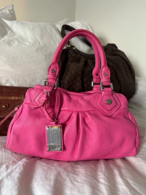 Marc by Marc Jacobs rosa handväska - Så söt rosa handväska i äkta läder från Marc by Marc Jacobs. Den ikoniska modellen Q Classic Baby Groove! En populär och eftertraktad vintagemodell med silverdetaljer och dubbla handtag. Långa bandet finns ej. Som ny!🤍  Mått: 34x18x12 cm (undersida) Kan hämtas hemma hos mig i Nacka eller skickas 🤍 