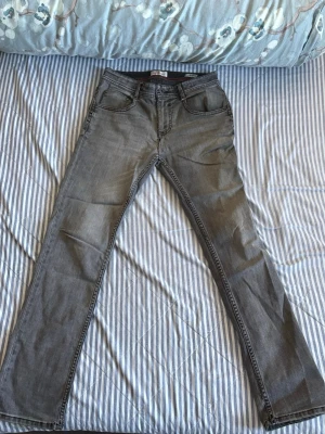 Grå raka jeans från Vingino - Säljer ett par grå jeans från Vingino med raka ben och klassisk femficksmodell. Jeansen har snygga slitningar och detaljer med små italienska flaggor vid fickorna. Materialet är mjukt denim som känns bekvämt hela dagen.