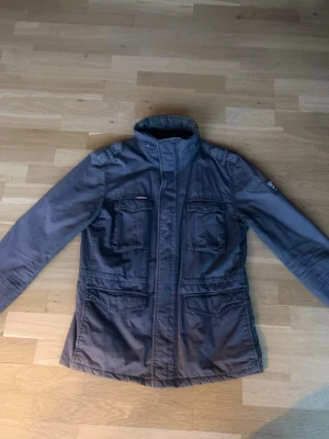 Mörkblå jacka med fickor - Snygg mörkblå jacka med hög krage och fyra framfickor. Jackan har dragkedja framtill och långa ärmar. Perfekt för dig som vill ha en stilren och praktisk jacka till vardags.