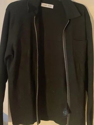Svart overshirt från Samsøe Samsøe - Stilren svart overshirt från Samsøe Samsøe  med klassisk krage och dragkedja framtill. Jackan har lång ärm och en diskret bröstficka. Perfekt för lager på lager och enkel att matcha med olika outfits.