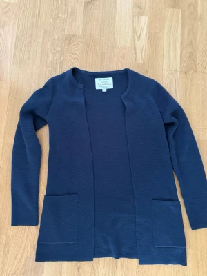 Mörkblå lång kofta med fickor - Stilren mörkblå lång kofta från Bread & Boxers. Koftan har öppen front, två stora fickor framtill och är tillverkad i ett mjukt, stickat material. Perfekt för lager på lager och enkel att matcha med olika outfits.