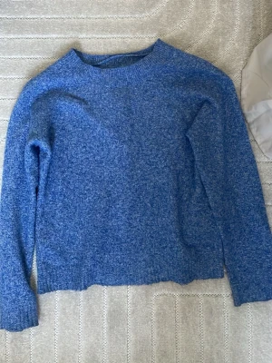 Blå stickad tröja från Vero Moda - Mysig blåmelerad stickad tröja från Vero Moda med rund halsringning och långa ärmar. Perfekt för kyliga dagar och enkel att matcha med jeans eller kjol. Materialet är mjukt och bekvämt, vilket gör den skön att bära hela dagen.