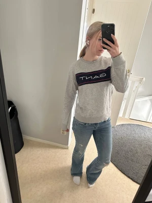 Grå sweatshirt från GANT - Säljer en grå sweatshirt från GANT med stor logga framtill i mörkblått och rött. Tröjan har rund halsringning, långa ärmar och ribbade muddar vid ärmslut och nederkant. Perfekt för en avslappnad och stilren look.
