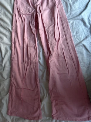 Vida rosa jeans med hög midja - Snygga ljusrosa jeans med vida ben och hög midja. Klassisk femficksmodell och raka sömmar. Perfekta för dig som vill sticka ut med färg och gillar en avslappnad, trendig look. Materialet känns mjukt och följsamt, vilket gör dem bekväma hela dagen.