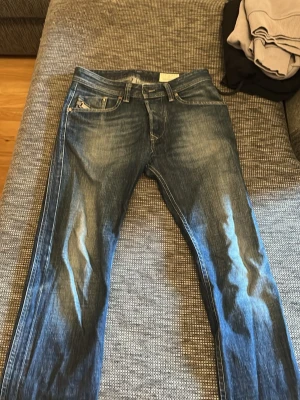 Blåa  jeans från Diesel - Säljer ett par blåa jeans från Diesel med slitningar och snygg tvätt. Klassisk femficksmodell med detaljerad söm och logga på myntfickan. Jeansen är i ett mjukt denimtyg och har en avslappnad passform.