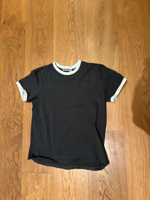 Svart t shirt från weekday  - Säljer den här trendia, snygga, svarta t shirten från Weekday, med vita detaljer runt ärmen och kragen, storlek S. Mycket bra skick, skriv vid eventuella funderingar😄