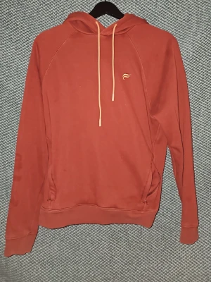 Fabletics hoodie  - Snygg hoodie i rostfärg från Fabletics med broderad logga på bröstet. Hoodien har huva med beige dragsko och en klassisk känguruficka framtill. Tillverkad i mjuk bomullsblandning som känns skön mot huden. Perfekt för en avslappnad och trendig stil. Är öppen för prisförslag vid snabb försäljning. Köpt i London 2022. Men fint använd.