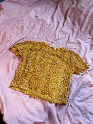 Gul spetsblus från Zara Trafaluc - Säljer en superfin gul spetsblus från Zara Trafaluc. Blusen är kortärmad och har ett genombrutet spetsmönster som ger en unik och trendig look. Perfekt att styla med ett linne under eller som den är för en cool vibe.