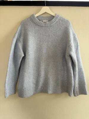 Ljusblå stickad tröja från Zara - Mysig ljusblå stickad tröja från Zara med rund halsringning och ribbade muddar vid ärmslut och nederkant. Tröjan har en avslappnad passform och är perfekt för lager på lager. Materialet är mjukt och ger en chill vibe.