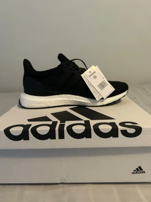 Svarta Adidas Ultra Boost sneakers - Säljer ett par svarta Adidas Ultra Boost sneakers med vit sula och klassiska tre ränder på sidan. Ovandelen är i ventilerande mesh och skon har en bekväm Boost-mellansula. Perfekta för dig som gillar stilrena och sportiga sneakers.