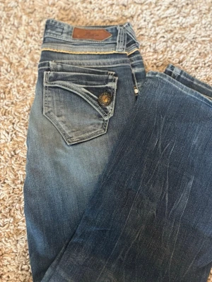 Blåa bootcut jeans - Blåa boorcut jeans från Back Number med fina beige detaljer vid fram fickorna. Jeansen har snygga Knappfickor som är användbara. Mått: Midjemått tvärs över knappen 40cm. Från grenen upp till linningen 21cm. Innebenslängden 74cm. Yttebenslängden 96cm. Hör av dig om du har frågor eller funderingar❤️