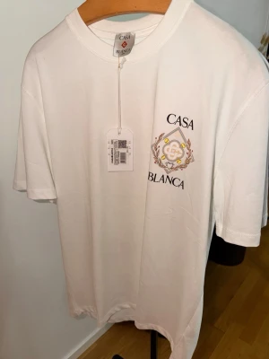 Vit Casa Blanca t-shirt med tryck - Snygg vit t-shirt från Casa Blanca med ett stilrent tryck på bröstet i form av logga och text. Klassisk rund halsringning och korta ärmar. Tillverkad i mjuk bomull som känns skön mot huden. Perfekt för dig som gillar minimalistisk och trendig stil.