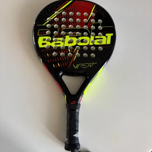 Babolat Viper padelracket - Knappt använd. Säljer ett Babolat Viper padelracket i svart, rött och neongult med tydlig logga och mönster. Racketen har perforerad träffyta och greppvänligt handtag. Tjocklek 38 mm står på sidan. Perfekt för dig som vill ta ditt padelspel till nästa nivå.