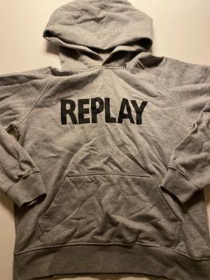 Grå hoodie från Replay - Snygg grå hoodie från Replay med stor svart logga på bröstet. Klassisk känguruficka framtill och huva. Mjuk bomullskänsla och avslappnad passform, perfekt för en chill look.