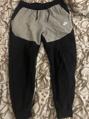 Nike mjukisbyxor svart och grå - Snygga och populära Nike Tech mjukisbyxor i svart och grå – perfekt mix av stil och komfort 🔥 Storlek M men sitter mer som en S (tight och snygg passform). I bra skick och väldigt sköna att bära. En liten defekt finns (se bild 2), men inget som stör helhetsintrycket eller funktionen. Perfekta till både vardag och träning. Säljes endast eftersom de tyvärr inte kommer till användning. Passa på att fynda endast 249 kr! 💯packas och skickas samma dag ( eller dagen efter) 