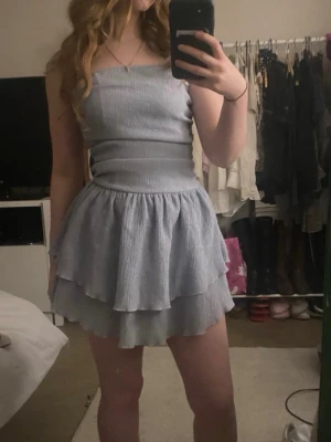 Ljusblå volangklänning  - Söt ljusblå kortklänning med smockad överdel och dubbla volanger i kjolen. Klänningen är ärmlös och har en figurnära passform upptill med en luftig kjol. Perfekt för sommarens alla tillfällen. HELT NY också! Prislappen sitter ej på.