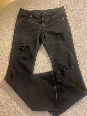 Svarta ripped jeans från Divided - Säljer ett par svarta jeans från Divided med slitningar på låren och knäna. Jeansen har klassisk femficksmodell och raka ben. Materialet är mjukt denim med stretch för extra komfort. Perfekta för en avslappnad och trendig look.