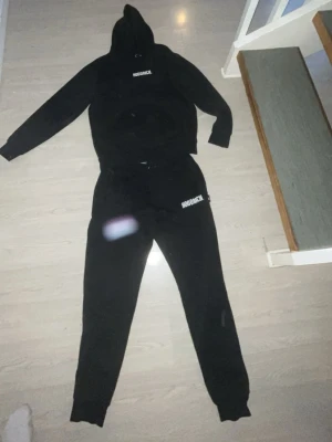 Svart Hoodrich set med logga - Säljer ett svart set från Hoodrich med matchande hoodie och byxor. Båda delarna har vit Hoodrich-logga tryckt på bröstet och benet. Setet har en avslappnad passform och är tillverkat i mjukt material, perfekt för en chill och streetwear-inspirerad look.