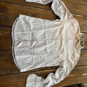 Blå linneskjorta Riley - Säljer en stilren blå skjorta från Riley i linne med klassisk krage och vita knappar framtill. Skjortan har lång ärm och en avslappnad passform, perfekt för en clean och enkel look. Passar till både jeans och chinos.