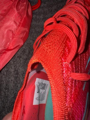 Nike Mercurial röda fotbollsskor - Säljer ett par Nike Mercurial fotbollsskor i en riktigt snygg röd färg med turkosa detaljer och snörning. Ovandelen är i ett lätt och ventilerande syntetmaterial som ger bra bollkontroll. Skorna har en modern, strömlinjeformad design och kommer med en matchande röd påse.