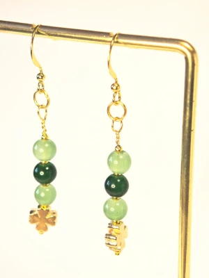 Guldiga örhängen med gröna pärlor st patricks day paddys - Unika handgjorda örhängen med guldfärgade krokar och detaljer. Tre runda pärlor i olika gröna nyanser pryder varje örhänge, avslutade med en liten fyrklöver i metall. Perfekta för dig som gillar färg och personliga accessoarer.